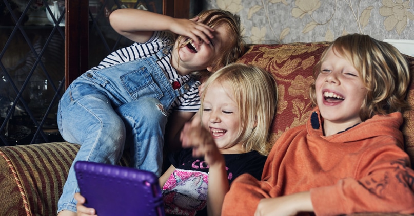 tre barn sitter og ler av en video på en ipad