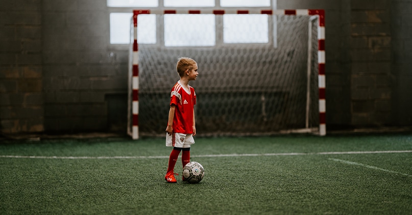 Liten gutt står i fotballdrakt med en fotball fremfor et fotballmål
