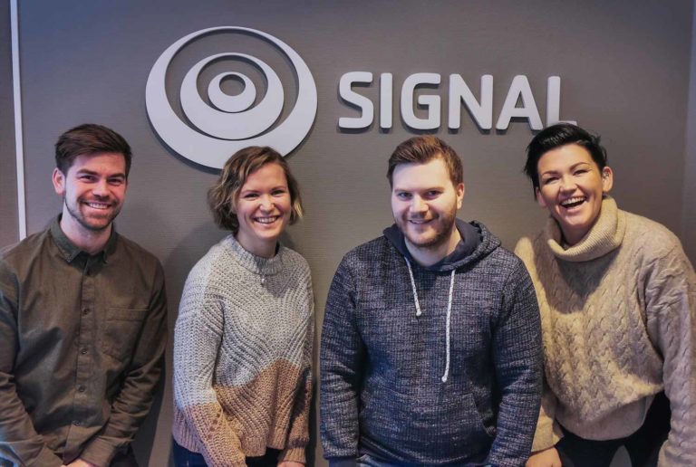 Fire ansatte fra kundesenteret i Signal Bredbånd i Alta står foran Signal-logoen på veggen