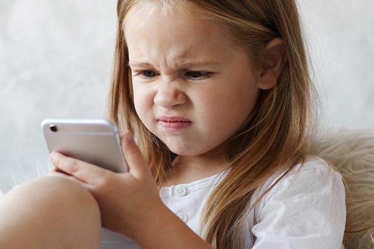 Liten jente skjærer en grimase mens hun ser på en mobil