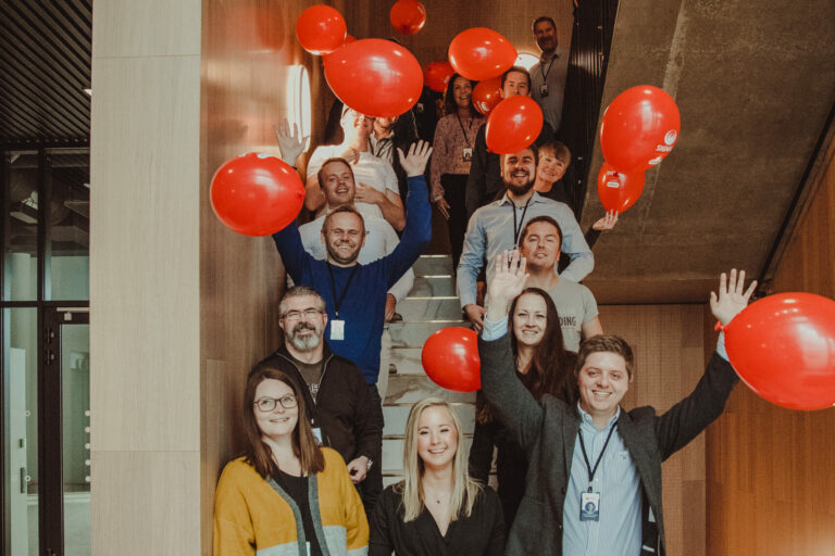En gjeng fra Signal står oppstilt i en trapp og feirer med røde ballonger