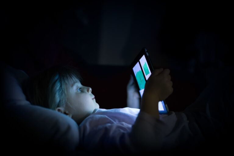 Liten jente ligger i mørket og ser på nettbrettet sitt