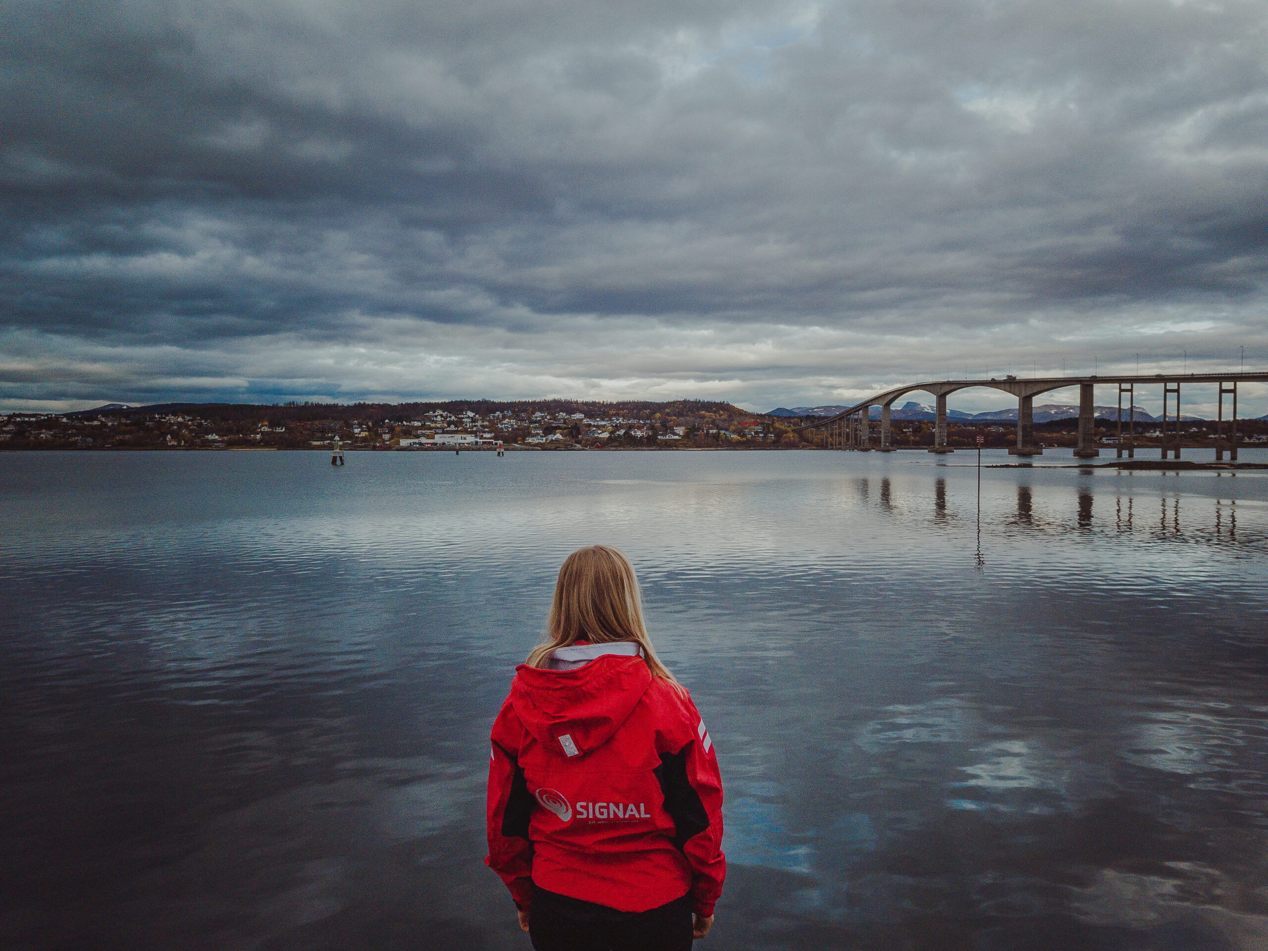 Jente i rød Signal-jakke ser ut over havet og brua mellom Finnsnes og Silsand