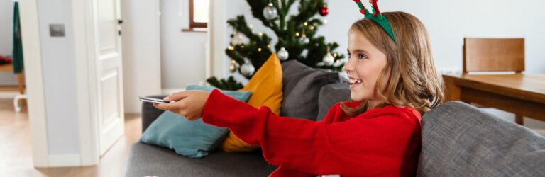 Julepyntet jente retter fjenkontrollen mot tv i spenning når hun slår på julefilm
