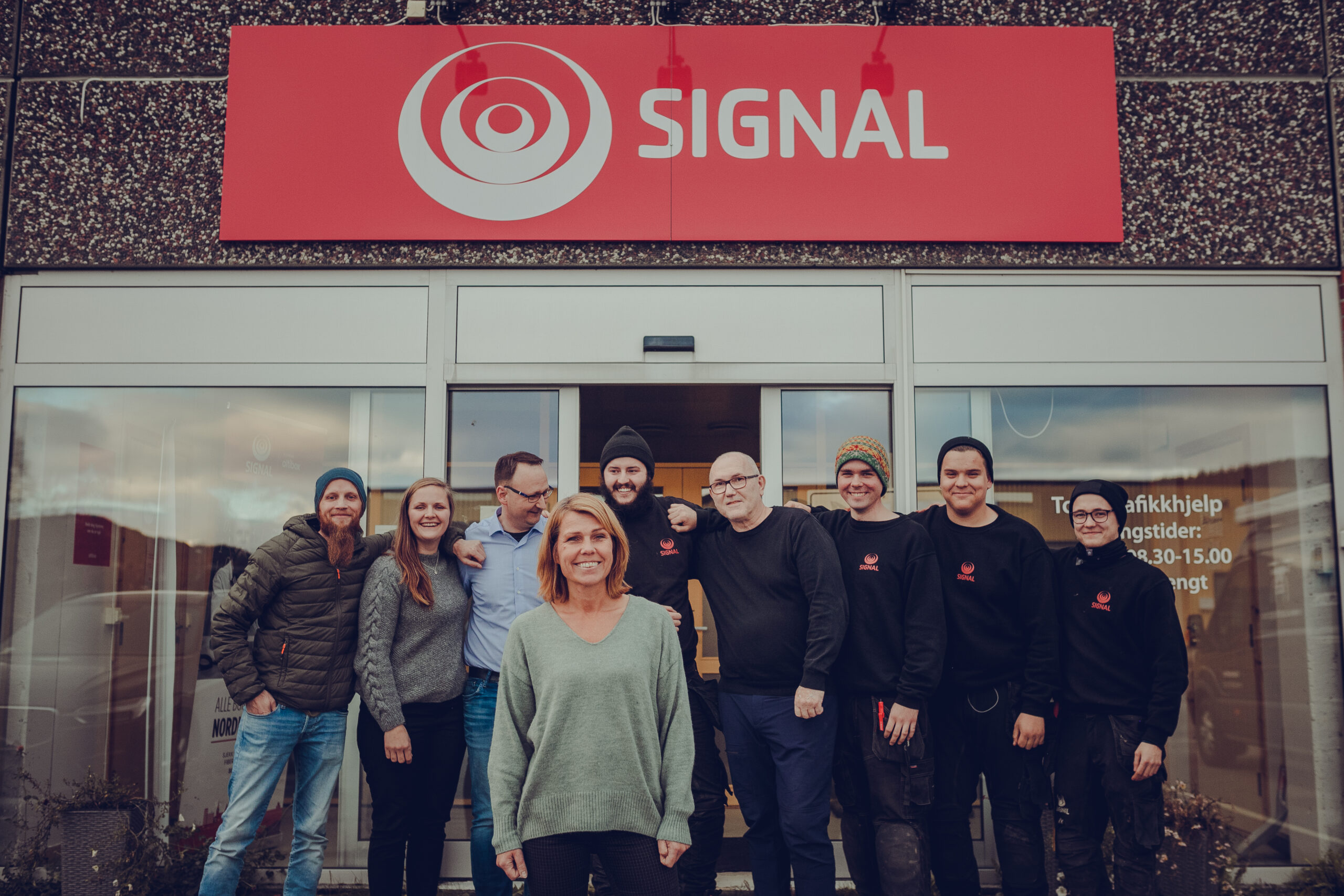 De ansatte i Signal Bredbånd avdeling Mosjøen står ved inngangspartiet under det røde Signal-skiltet.