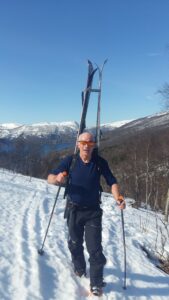 Kåre Berglund går med randonee-skiene på ryggen på snødekt landskap på vei opp et fjell