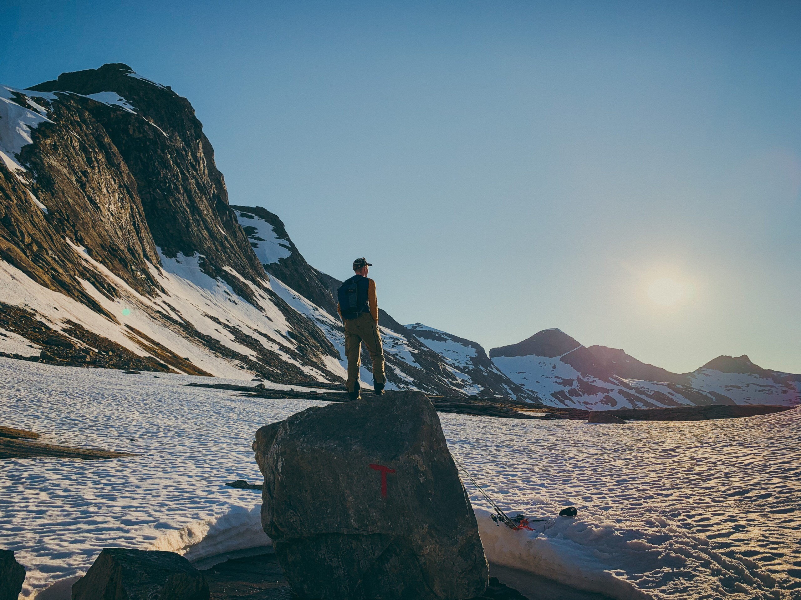Mann står på en turistforening-sten med fjell i bakgrunn og soler seg