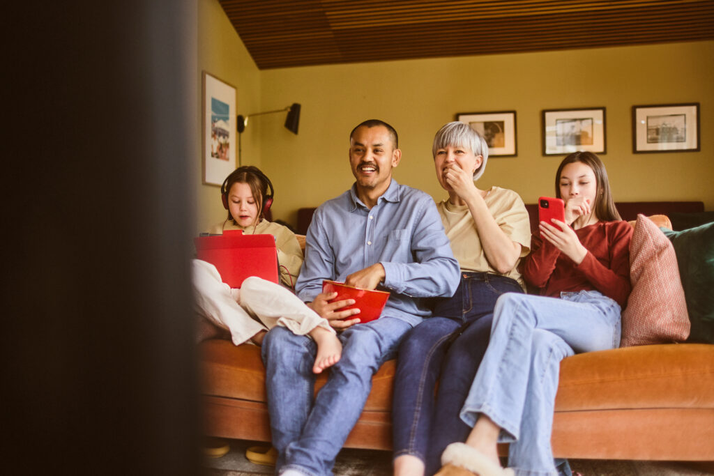 Familie som sitter i sofa med ulike digitale enheter.